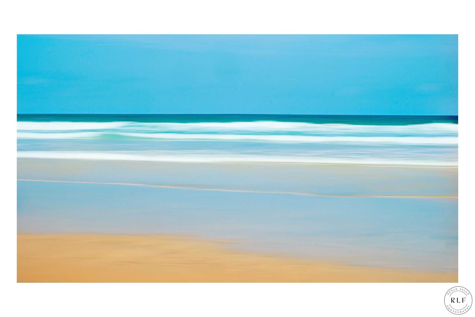 Soft, blurred coastal scene with blue sky, turquoise ocean, and sandy beach in warm tones.