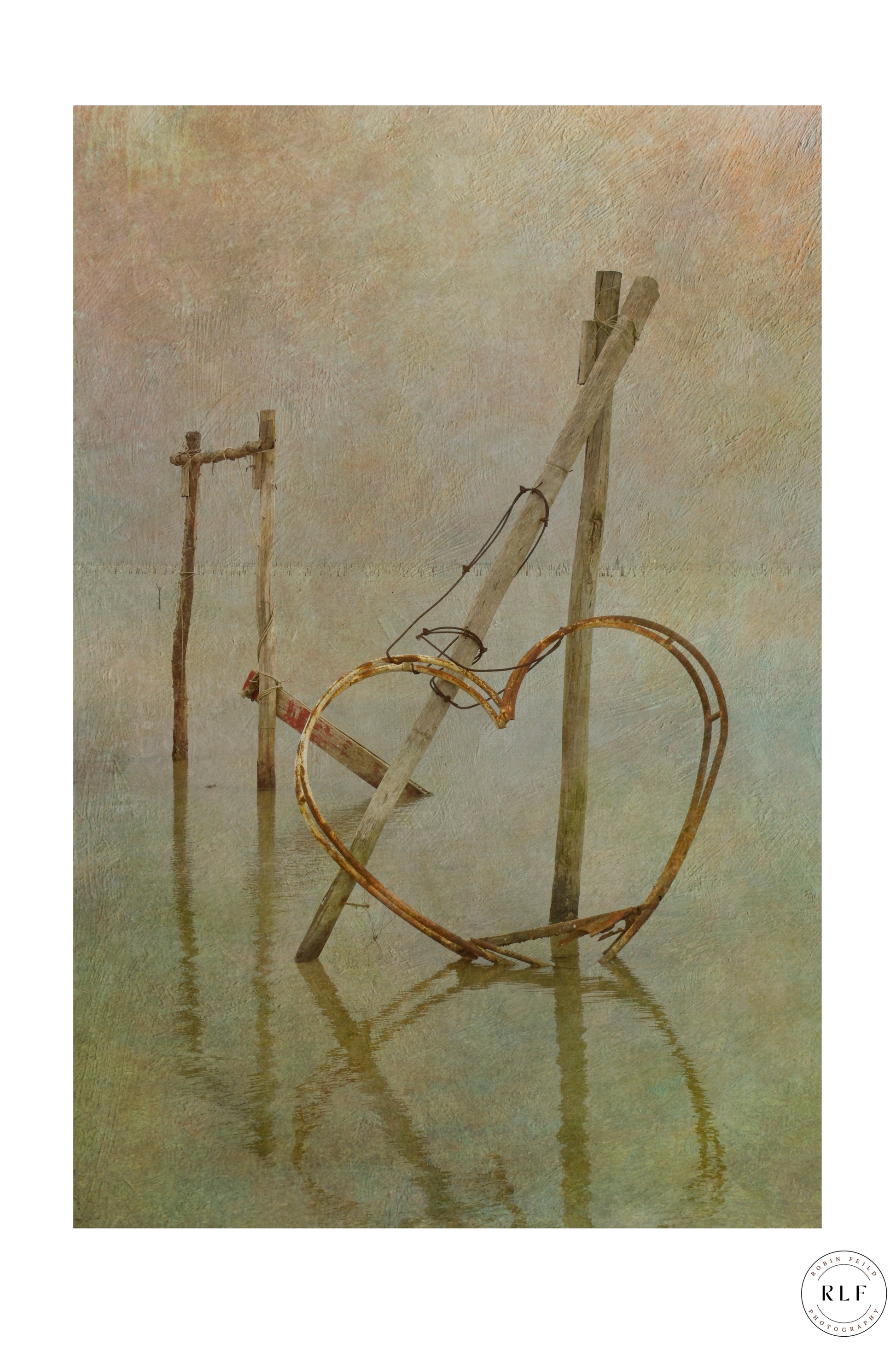 Rusted metal heart structure on wooden posts, partially submerged in calm lagoon water. Fine art photography by RLF Photography