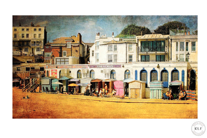 Colourful English seaside scene with pastel beach huts, people relaxing, and period houses in the background. Fine art photography by RLF Photography