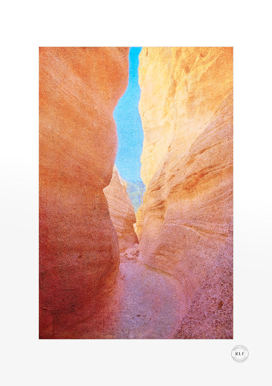 Winding slot canyon trail between warm red and golden sandstone walls, a thin ribbon of blue sky overhead, Tent Rocks, New Mexico. Fine art photography by RLF Photography