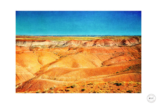 Vibrant Arizona desert scene with red and orange hills, sparse vegetation, and a clear blue sky.