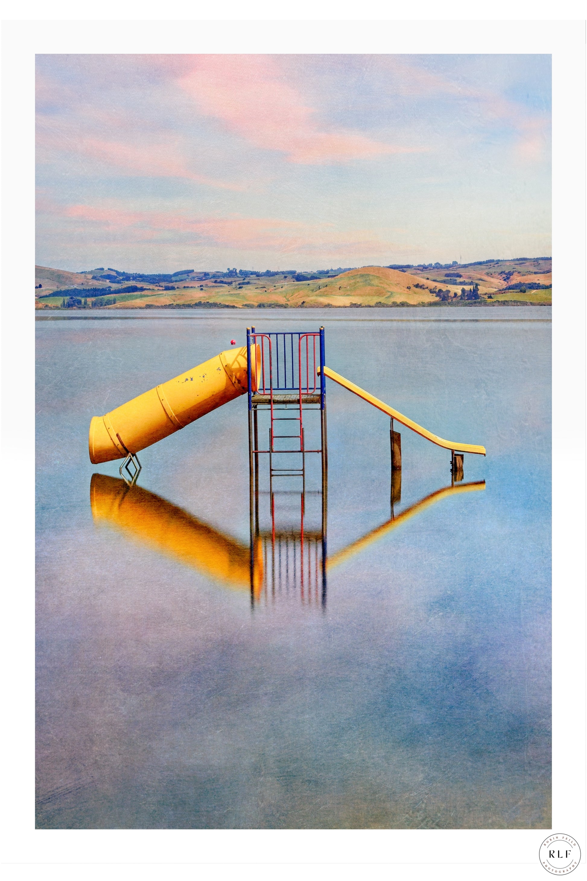 Fine art landscape photo of a colorful playground slide reflected in calm lwater with pastel sky and rolling hills — Fine Art Photography by RLF Photography