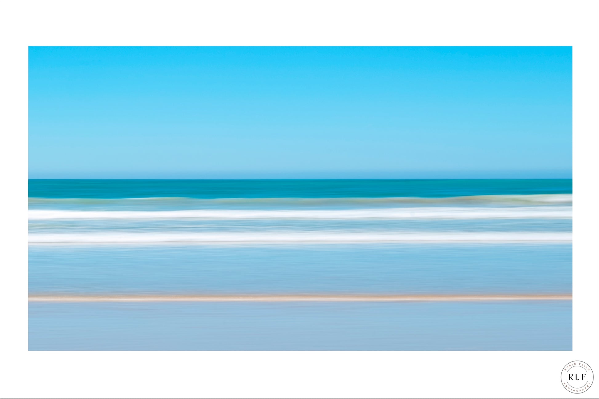 Soft, blurred coastal scene with gentle waves, blue sky, and sandy beach. Fine Art Photography by RLF Photography