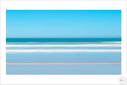 Soft, blurred coastal scene with gentle waves, blue sky, and sandy beach. Fine Art Photography by RLF Photography