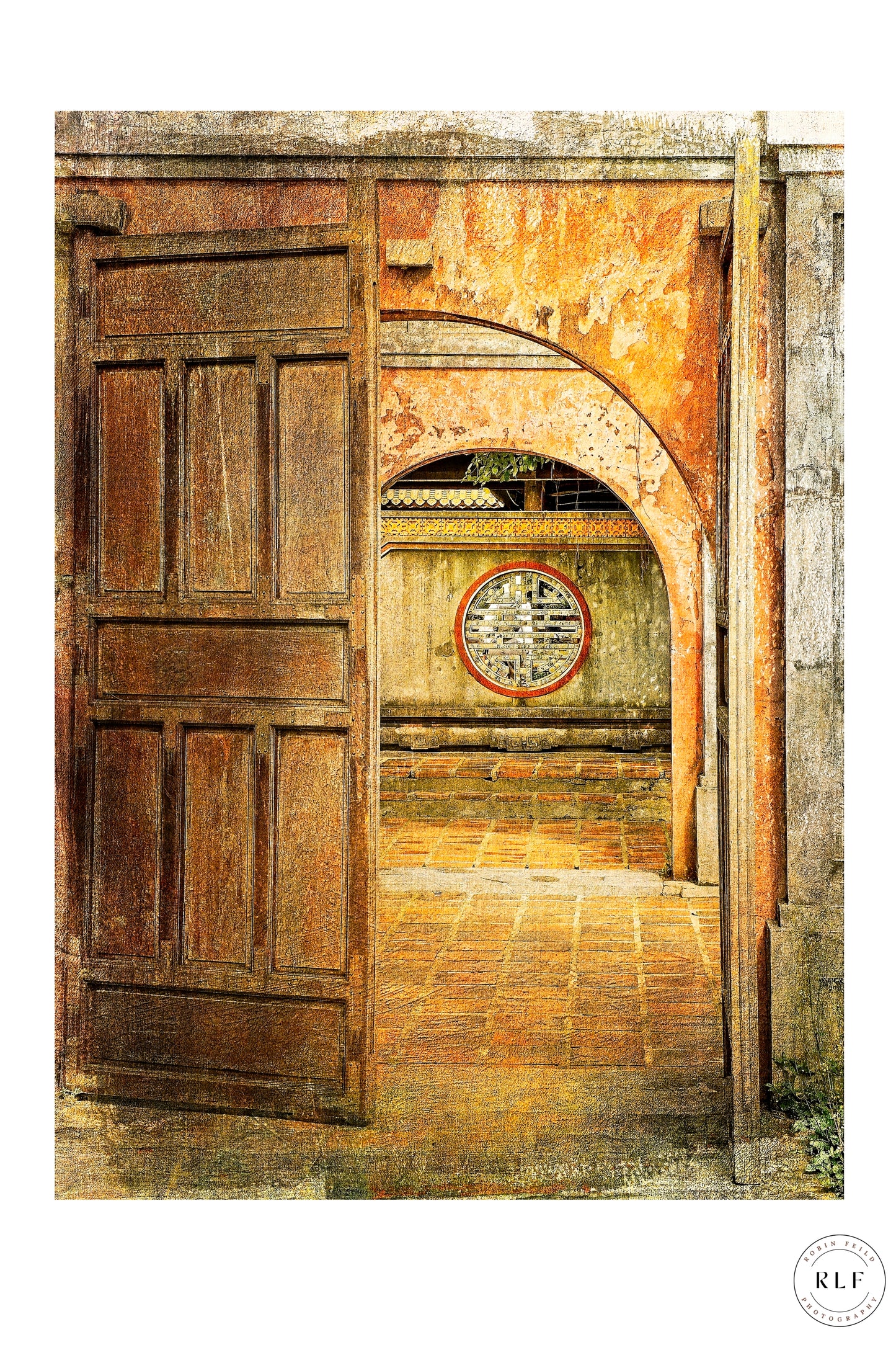 Open doorway in a Vietnamese temple, with ancient symbol set into textured stone wall, soft natural light guiding the viewer’s gaze down a tranquil, timeworn pathway of terracotta flagstones. Fine art photography by RLF Photography