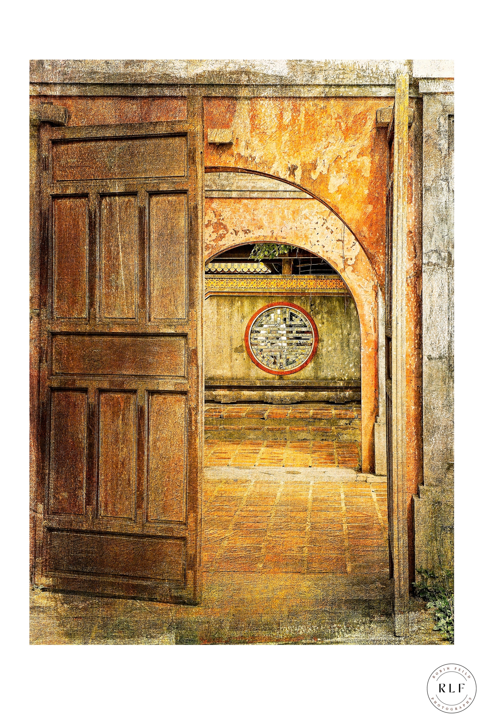 Open doorway in a Vietnamese temple, with ancient symbol set into textured stone wall, soft natural light guiding the viewer’s gaze down a tranquil, timeworn pathway of terracotta flagstones. Fine art photography by RLF Photography